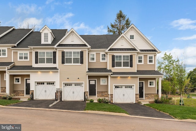 townhome / multi-family property with driveway, a standing seam roof, stone siding, metal roof, and a garage