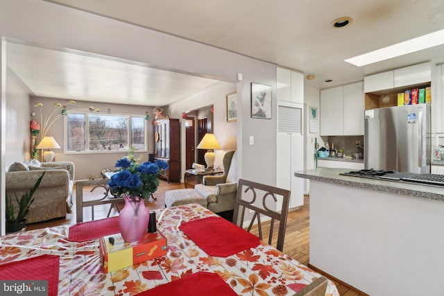 dining area featuring light wood finished floors, a skylight, and baseboards