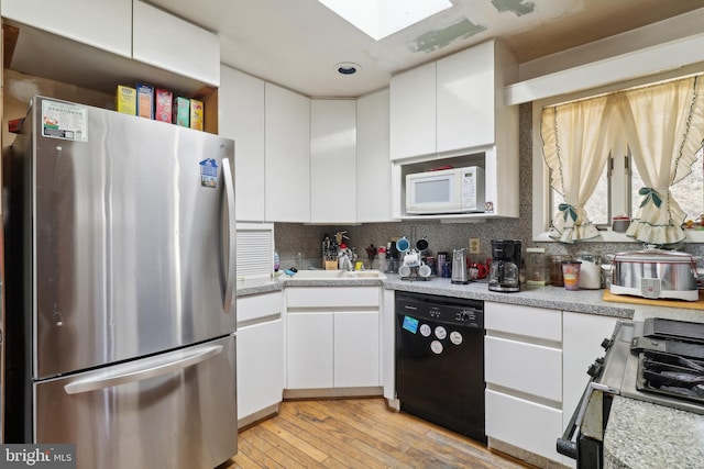 kitchen featuring a skylight, light countertops, white cabinets, appliances with stainless steel finishes, and light wood-type flooring