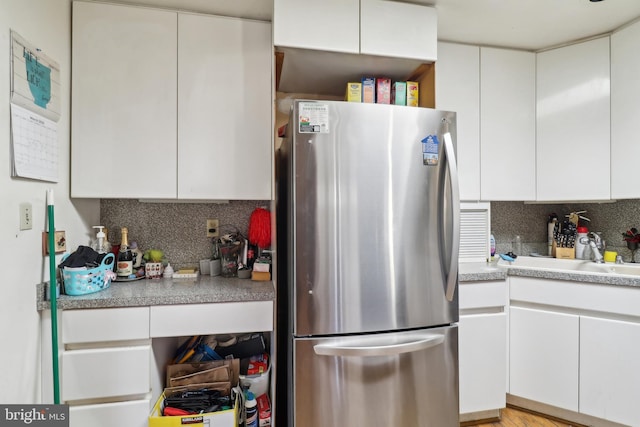 kitchen with a sink, white cabinetry, freestanding refrigerator, light countertops, and decorative backsplash