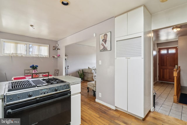 kitchen with black range with gas stovetop, white cabinetry, light wood-type flooring, and light countertops