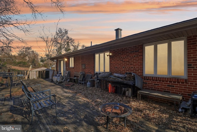 back of house with brick siding, a wooden deck, a fire pit, and an outbuilding