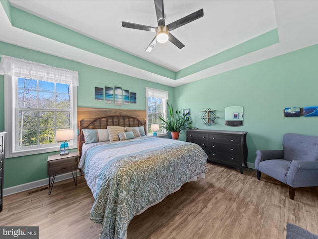 bedroom featuring a raised ceiling, wood finished floors, baseboards, and ceiling fan