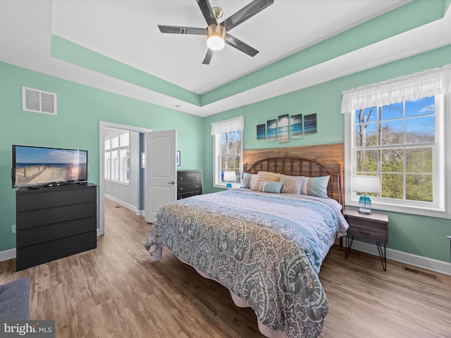 bedroom with visible vents, baseboards, a tray ceiling, and wood finished floors