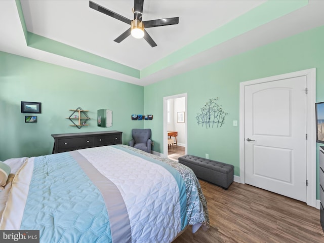 bedroom featuring a ceiling fan, a tray ceiling, wood finished floors, and baseboards