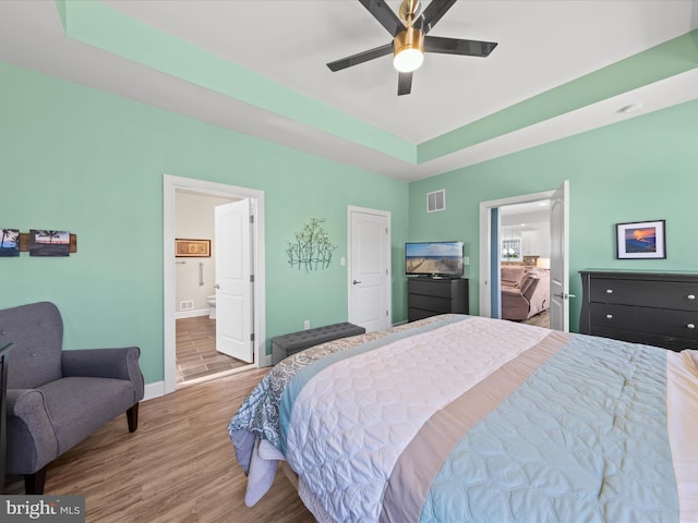 bedroom with visible vents, ensuite bathroom, wood finished floors, baseboards, and a raised ceiling