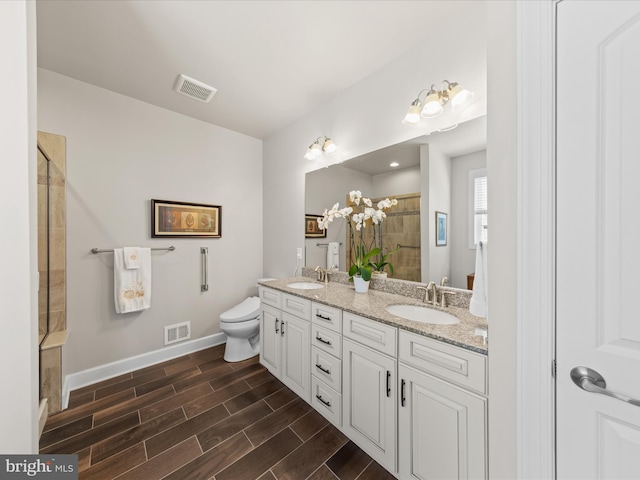 bathroom featuring visible vents, wood tiled floor, a stall shower, a sink, and toilet