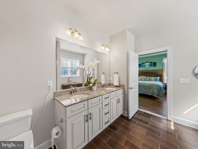 full bath featuring connected bathroom, wood finish floors, toilet, double vanity, and a sink