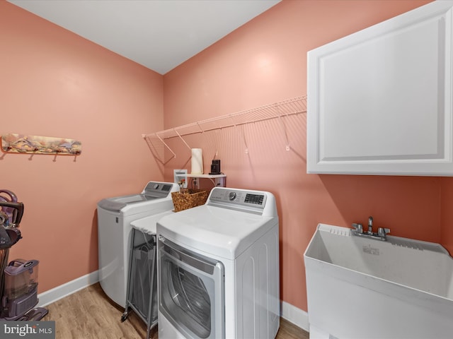 laundry room with washing machine and clothes dryer, baseboards, light wood-type flooring, cabinet space, and a sink