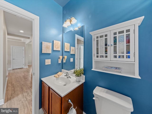 bathroom with toilet, vanity, baseboards, and wood finished floors