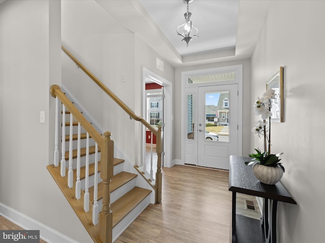 entryway featuring visible vents, baseboards, stairway, light wood-style floors, and a raised ceiling