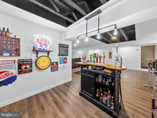 bar featuring track lighting, a bar, baseboards, and wood finished floors