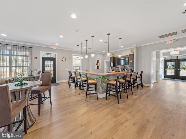 dining space featuring light wood finished floors, visible vents, ornamental molding, a wealth of natural light, and french doors