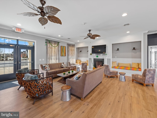 living room featuring a ceiling fan, crown molding, a lit fireplace, and wood finished floors