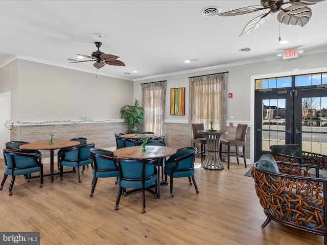 dining room featuring visible vents, crown molding, ceiling fan, a wainscoted wall, and wood finished floors