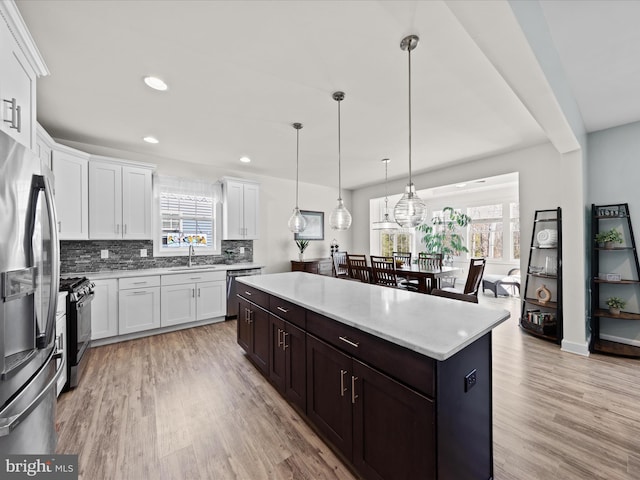 kitchen with backsplash, a kitchen island, light wood-style flooring, stainless steel appliances, and a sink