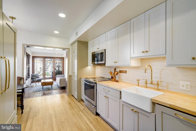 kitchen with light wood-type flooring, butcher block countertops, a sink, appliances with stainless steel finishes, and decorative backsplash