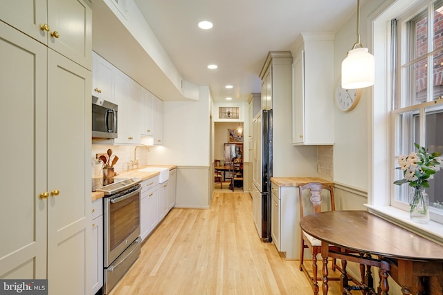 kitchen with light wood-style flooring, a sink, light countertops, appliances with stainless steel finishes, and tasteful backsplash