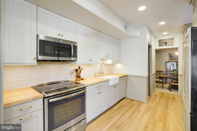 kitchen with light wood-style flooring, a sink, stainless steel appliances, wood counters, and tasteful backsplash