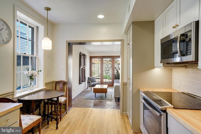 kitchen featuring decorative light fixtures, appliances with stainless steel finishes, light wood finished floors, decorative backsplash, and wooden counters