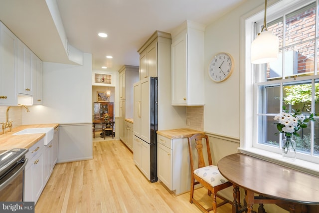 kitchen with a sink, decorative backsplash, stove, fridge, and light wood-type flooring