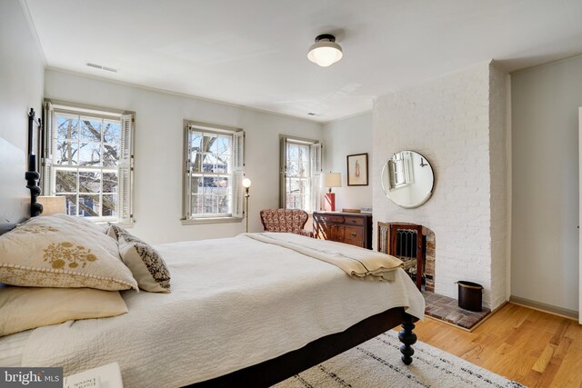 bedroom with visible vents, a brick fireplace, crown molding, baseboards, and wood finished floors