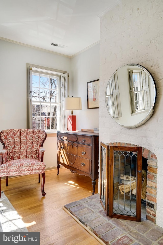 living area with a glass covered fireplace, visible vents, wood finished floors, and ornamental molding