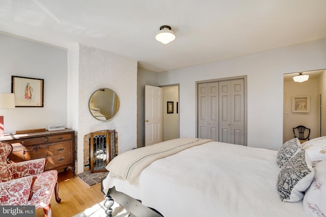 bedroom featuring a closet, a brick fireplace, and light wood-style floors