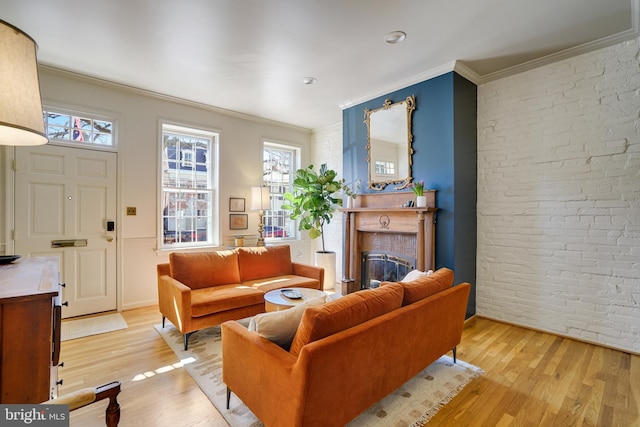 living room with a glass covered fireplace, brick wall, light wood-type flooring, and crown molding