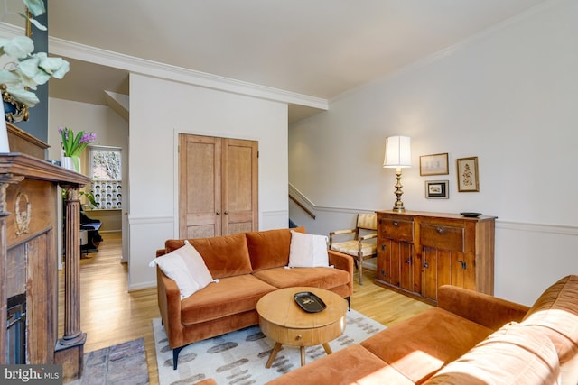 living area with light wood finished floors, stairway, a tiled fireplace, and crown molding