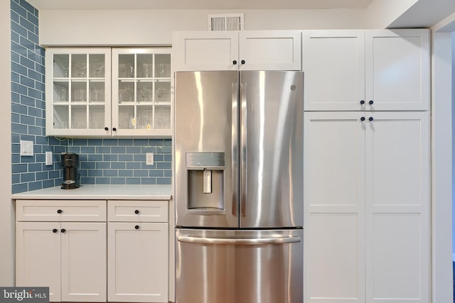 kitchen featuring visible vents, backsplash, stainless steel fridge, light countertops, and glass insert cabinets