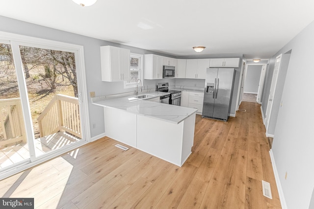 kitchen with visible vents, light stone countertops, appliances with stainless steel finishes, a peninsula, and a sink