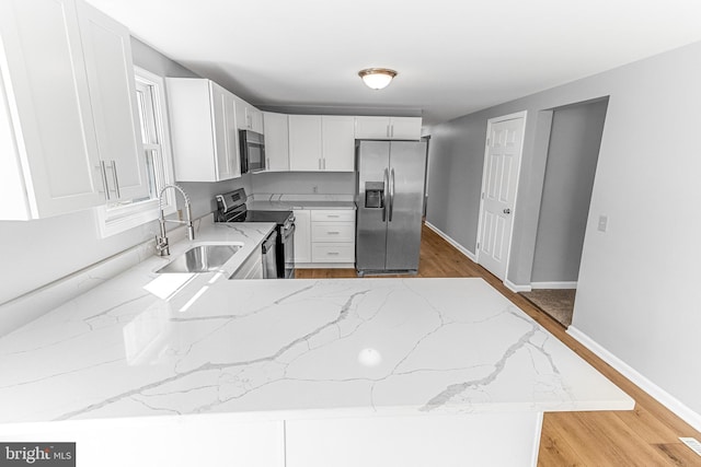 kitchen featuring light wood-style flooring, a sink, stainless steel appliances, white cabinets, and light stone countertops