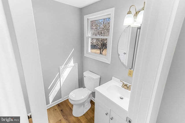 half bath with toilet, vanity, and wood finished floors