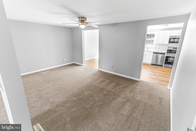 unfurnished living room with visible vents, light colored carpet, baseboards, and ceiling fan