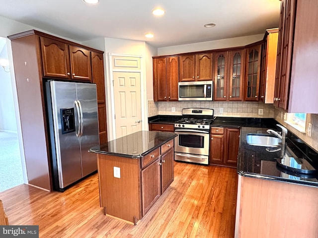 kitchen featuring appliances with stainless steel finishes, dark stone counters, light wood-type flooring, and a sink