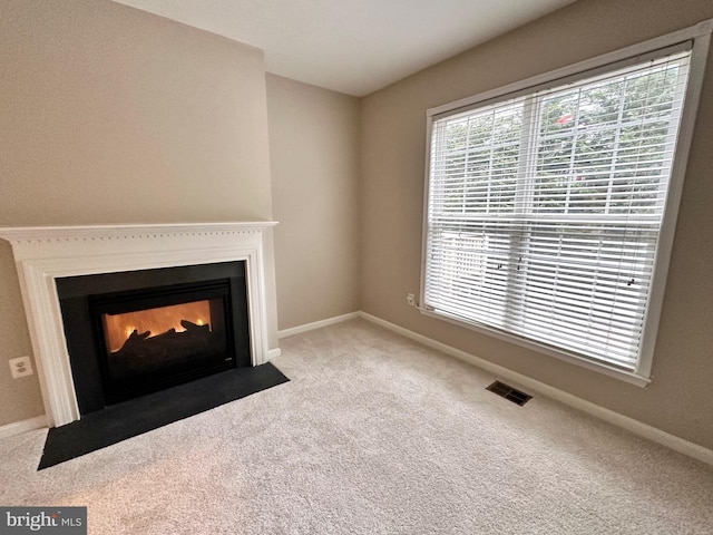 unfurnished living room with visible vents, a fireplace with flush hearth, carpet, and baseboards