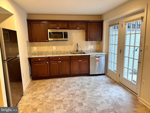 kitchen featuring a sink, stone finish flooring, tasteful backsplash, and appliances with stainless steel finishes