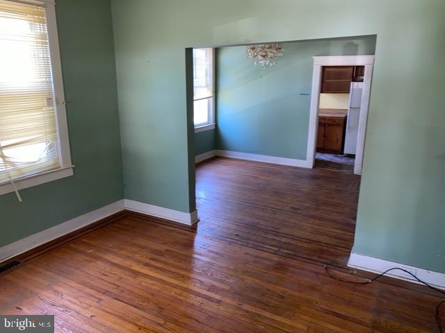 spare room featuring an inviting chandelier, baseboards, and wood finished floors