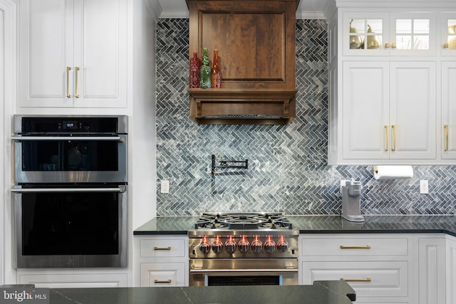 kitchen with white cabinets, glass insert cabinets, appliances with stainless steel finishes, dark countertops, and tasteful backsplash