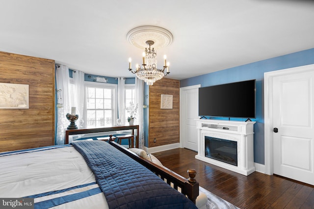 bedroom with baseboards, a notable chandelier, a glass covered fireplace, and hardwood / wood-style flooring