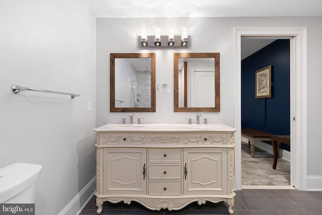 bathroom with double vanity, toilet, baseboards, and a sink