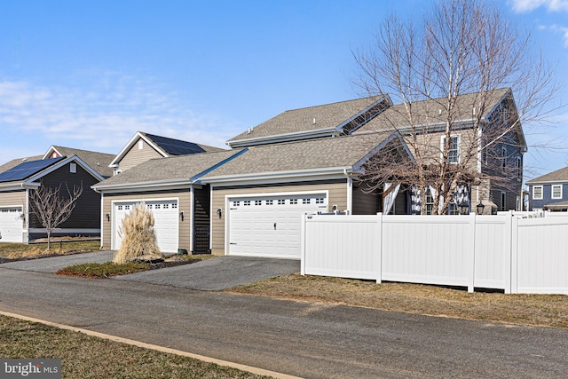 view of front of house with a garage, roof with shingles, and fence