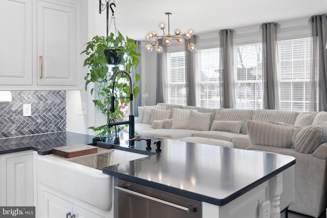 kitchen featuring backsplash, dark countertops, stainless steel dishwasher, open floor plan, and white cabinetry