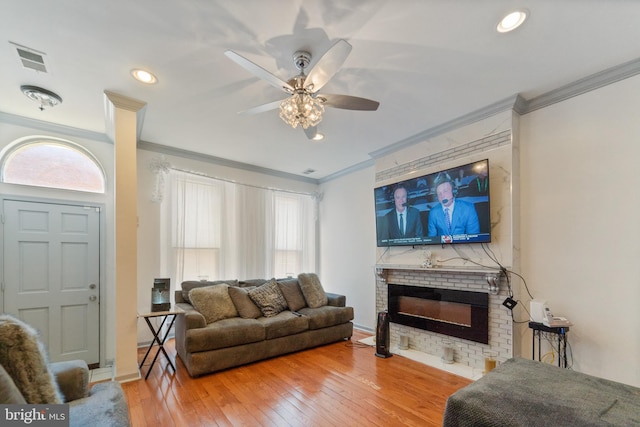 living room featuring visible vents, ornamental molding, hardwood / wood-style flooring, recessed lighting, and a brick fireplace