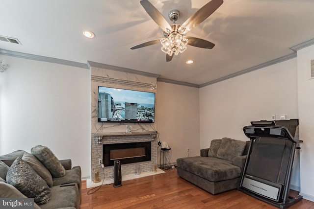 living area with a fireplace, crown molding, wood finished floors, and visible vents