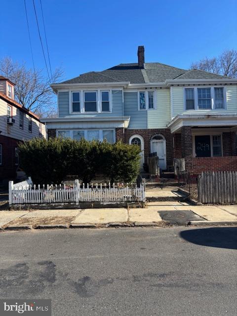 townhome / multi-family property featuring brick siding, a fenced front yard, and a chimney