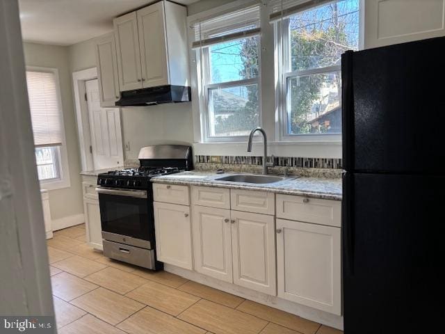 kitchen with stainless steel range with gas cooktop, freestanding refrigerator, a sink, white cabinets, and under cabinet range hood