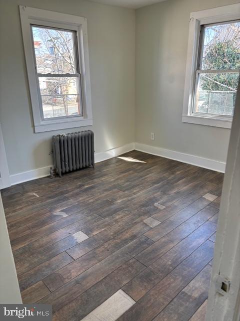 spare room featuring baseboards, radiator, and dark wood-style flooring