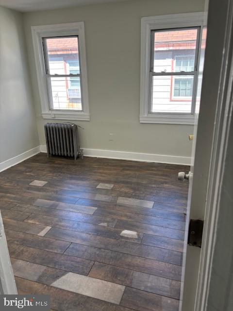 spare room with a wealth of natural light, radiator heating unit, baseboards, and dark wood-style flooring